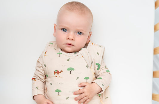 Baby lying in crib wearing 1 TOG bamboo baby sleep bag in camel print